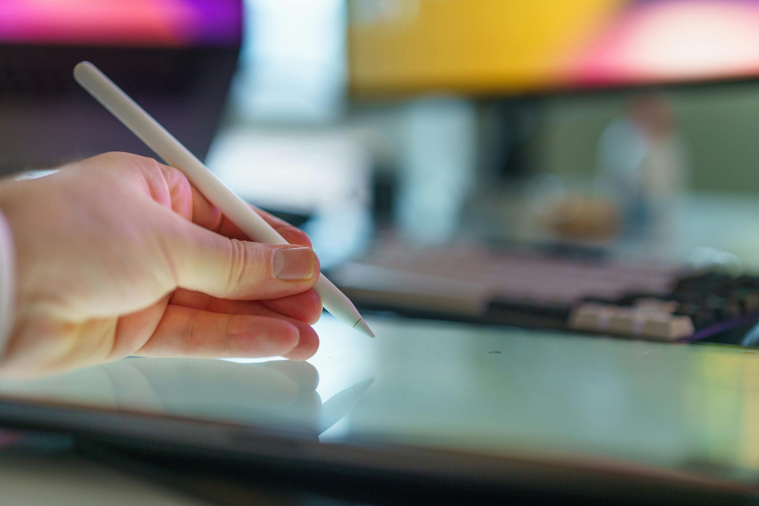 Close-up of a hand using a stylus on a digital drawing tablet in a creative home office setup.